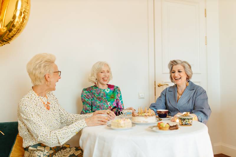 Three senior women sitting at a round table enjoying tea and cake at a social event in their community.